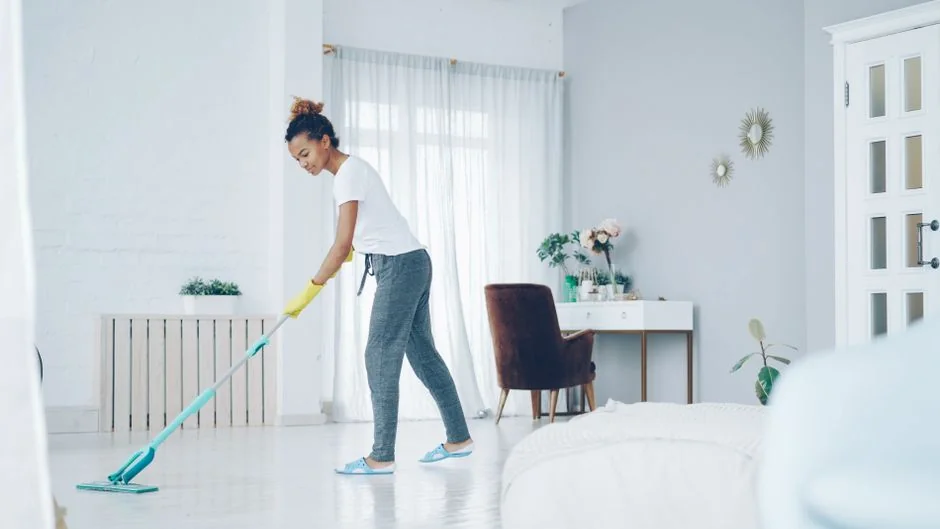 Two women in red overalls vacuuming and sweeping a modern living room.